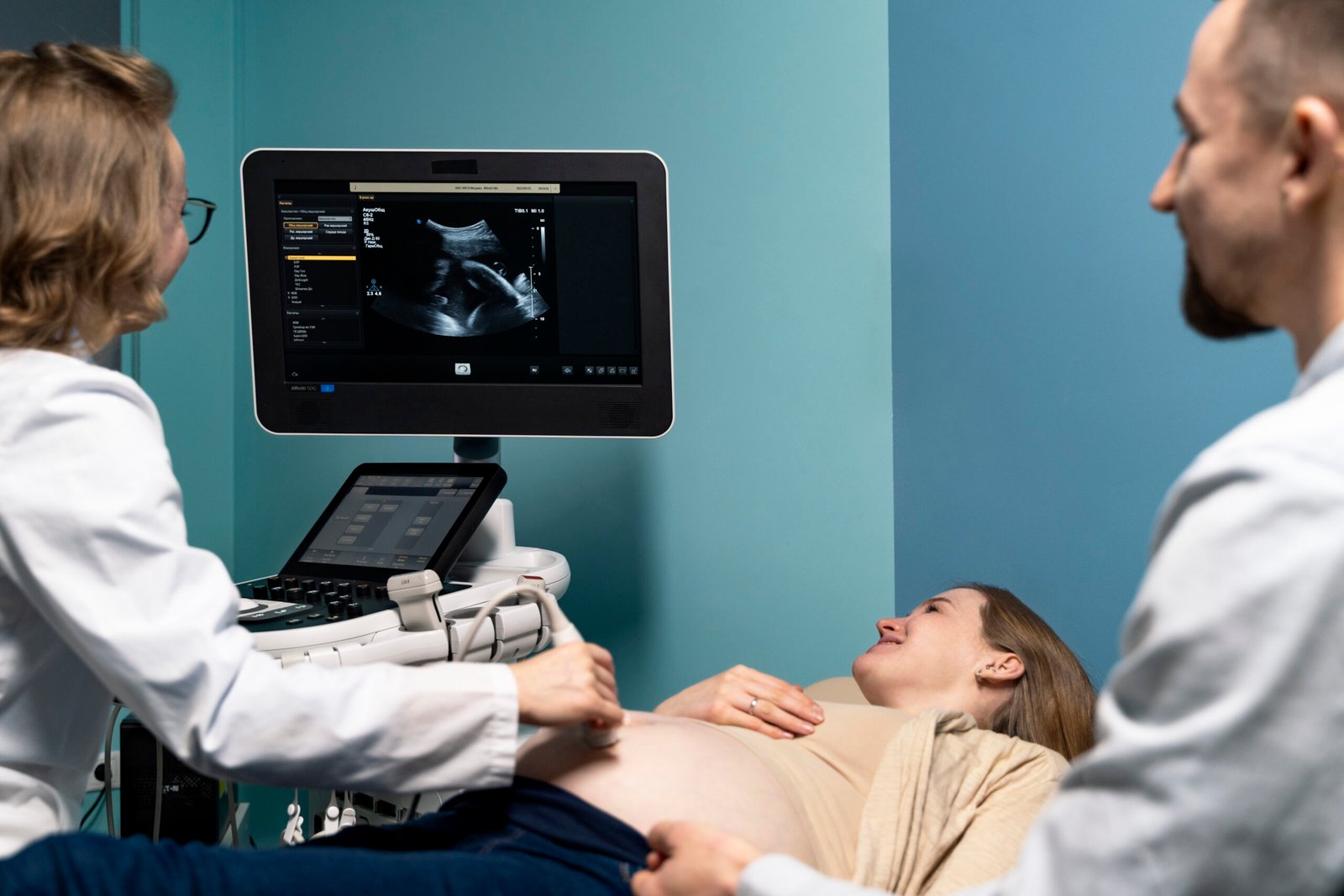 Doctor performing pregnancy ultrasound scan for expectant mother with partner in clinic
